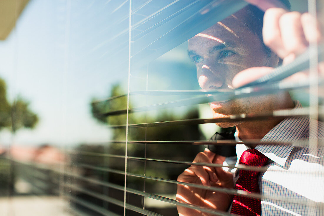 Businessman peering through window blinds