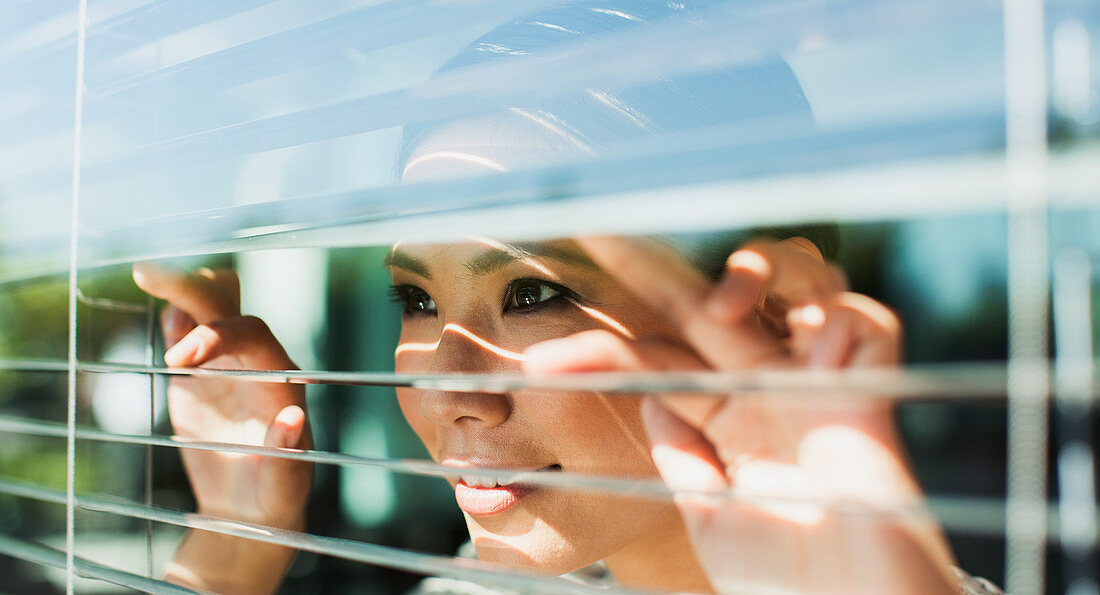 Businesswoman peering through window blinds