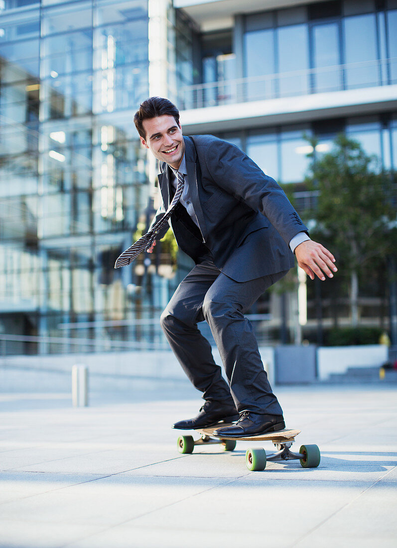 Smiling businessman skateboarding outside urban building