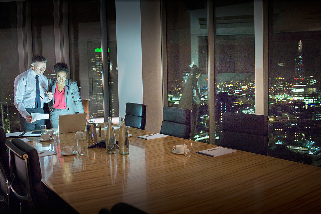 Business people at laptop in conference room at night