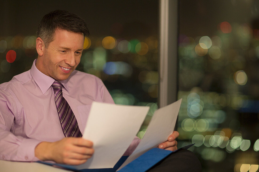 Businessman reading paperwork in office at night