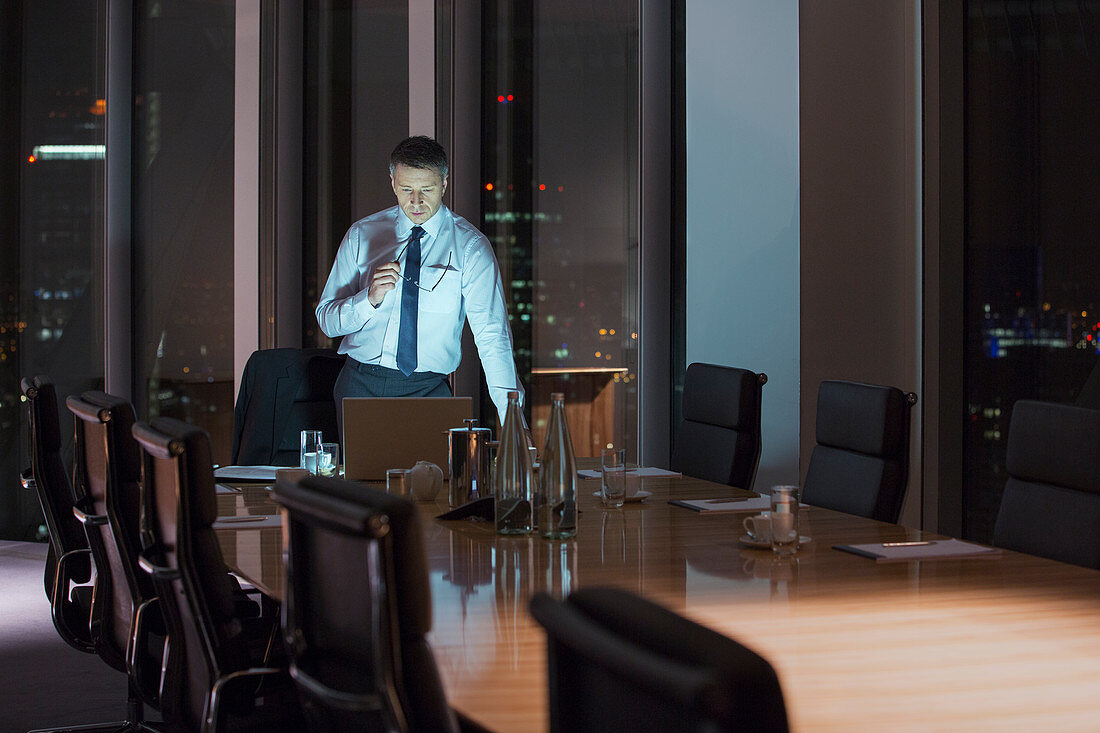 Businessman working at laptop in conference room at night