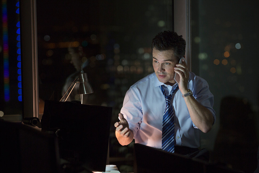 Businessman talking on cell phone in office at night