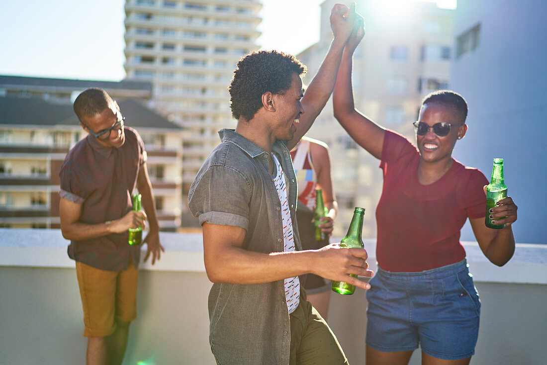 Young friends dancing and drinking beer on urban rooftop