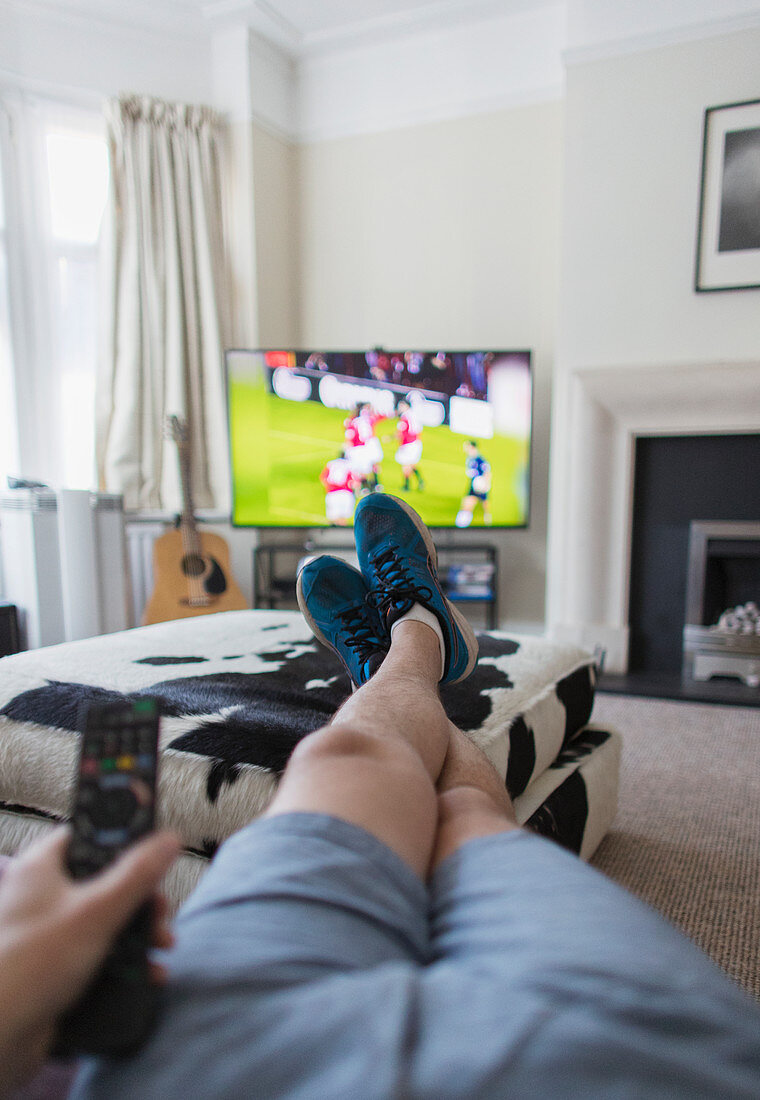 POV man watching soccer match on TV in living room