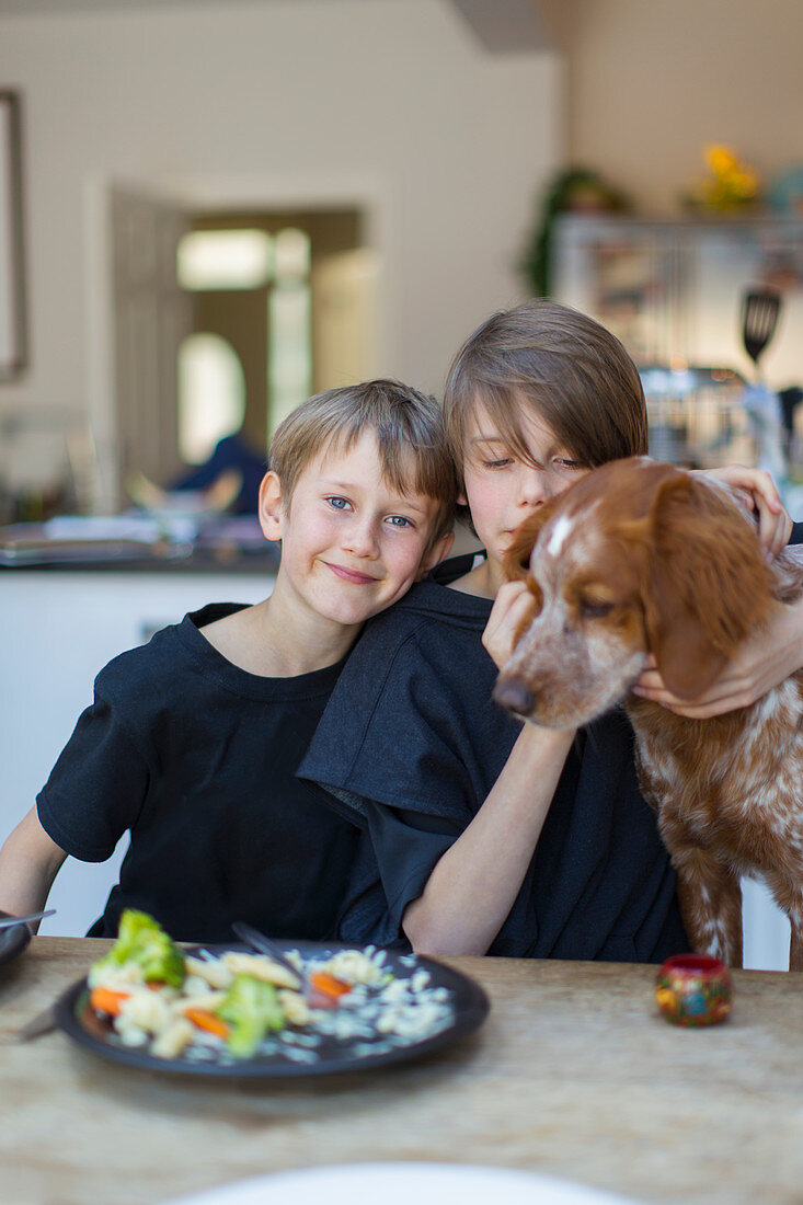 Portrait brothers with dog eating at dining table