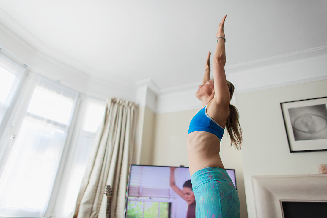 Woman practicing yoga online in living room