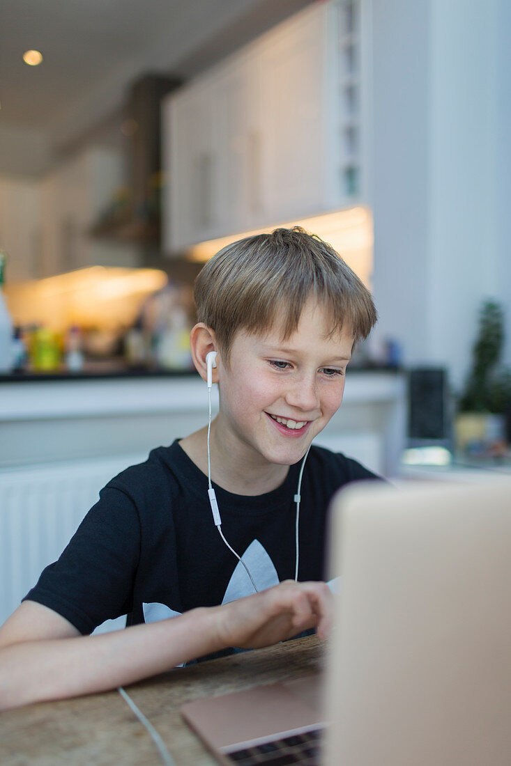 Smiling boy with headphones homeschooling at laptop
