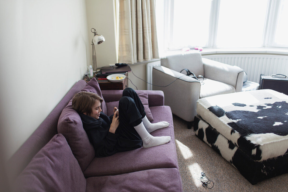Boy using smart phone on living room sofa