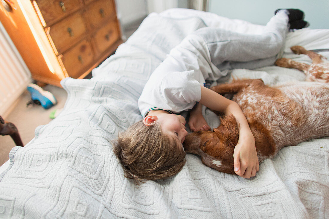 Affectionate boy cuddling dog on bed
