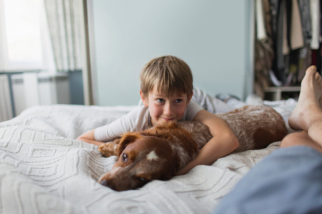 Cute boy cuddling with dog on bed