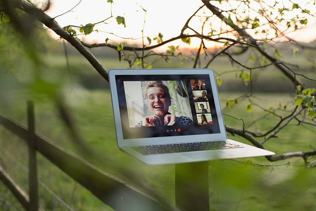 Friends video chatting on laptop screen on rural fence post