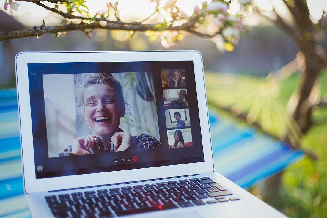 Friends video chatting on laptop screen in sunny garden