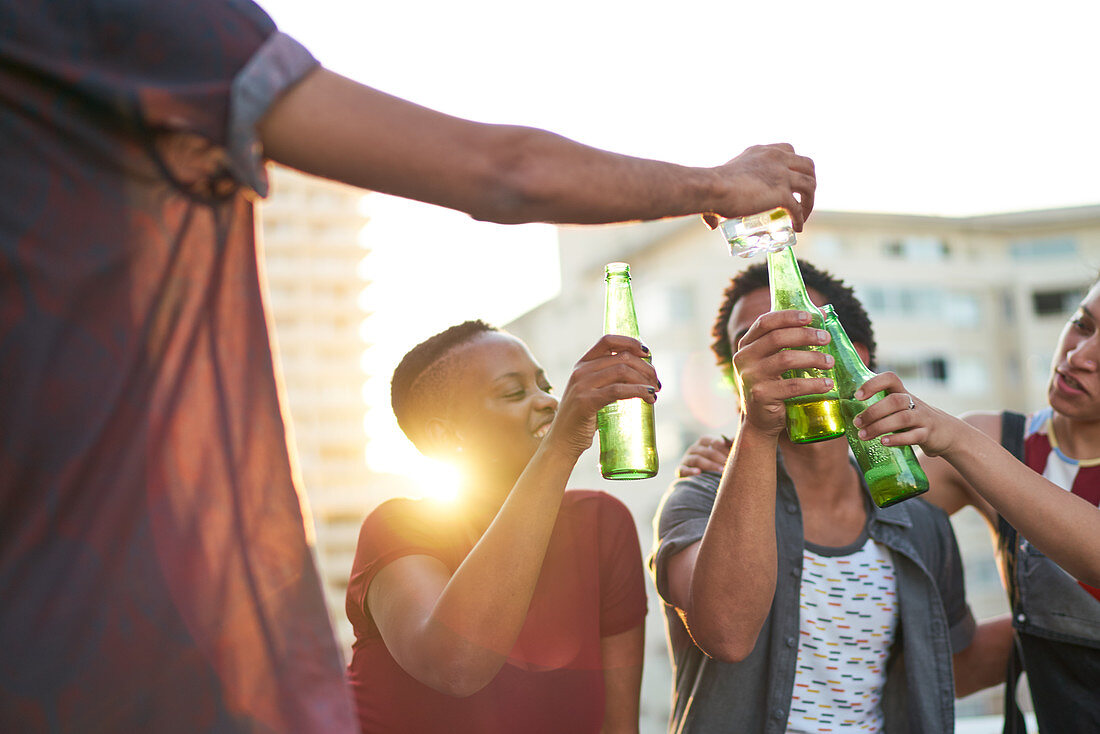 Young friends toasting beer glasses on sunny urban rooftop