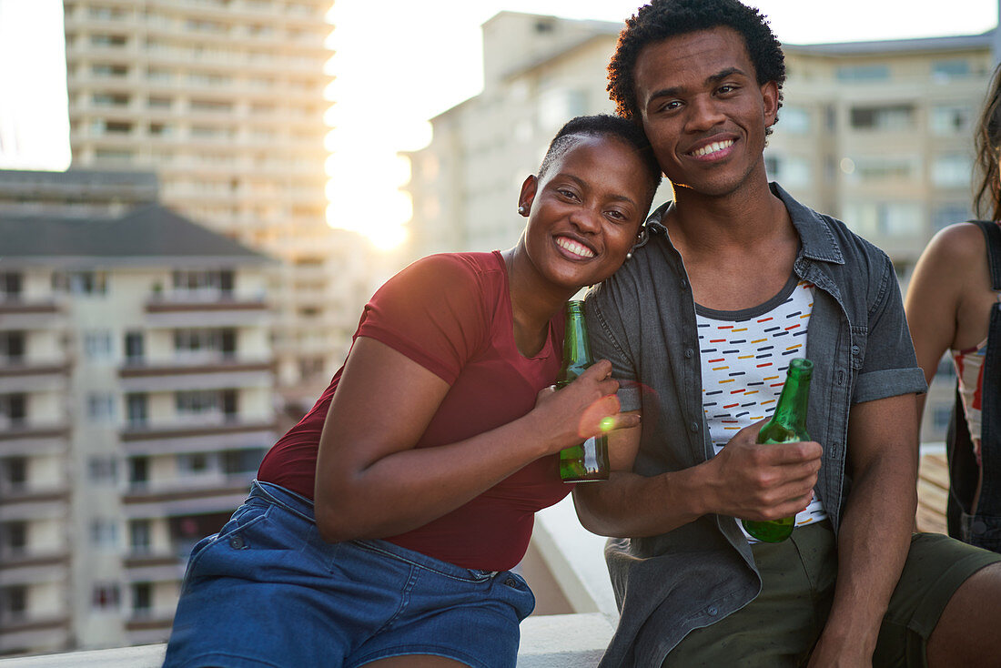 Portrait happy young couple drinking beer on urban rooftop