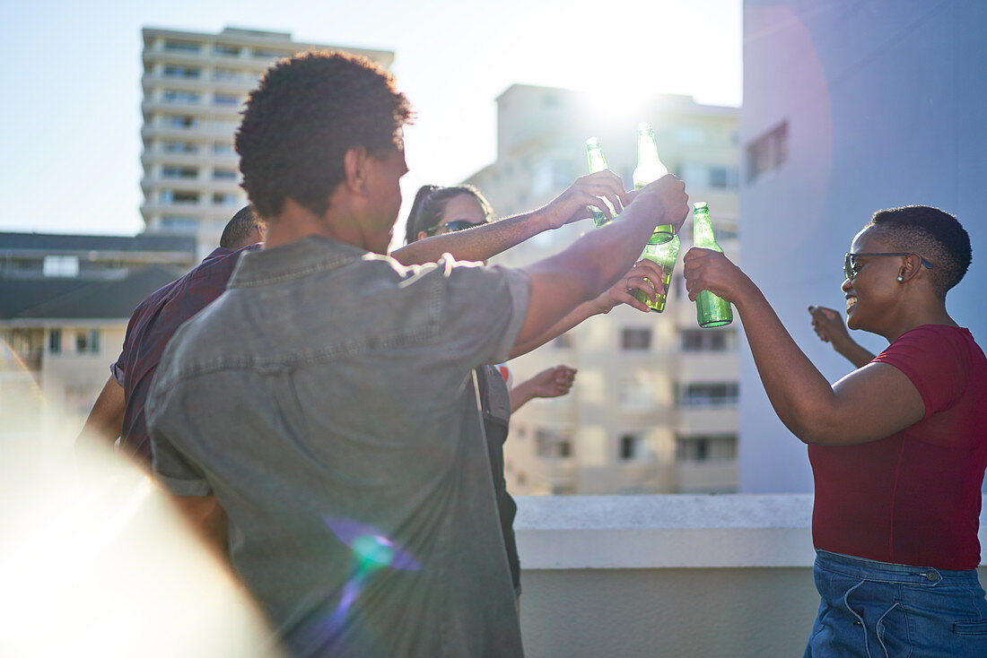 Young friends dancing and drinking beer on sunny rooftop