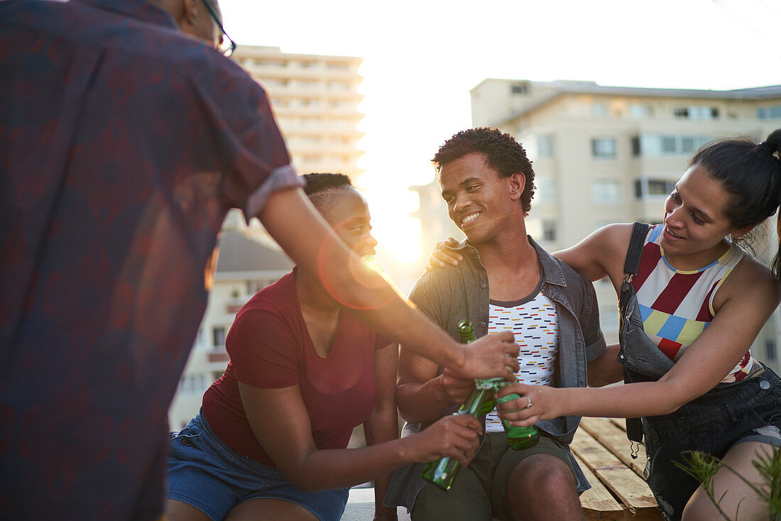 Young friends drinking beer on sunny urban rooftop balcony