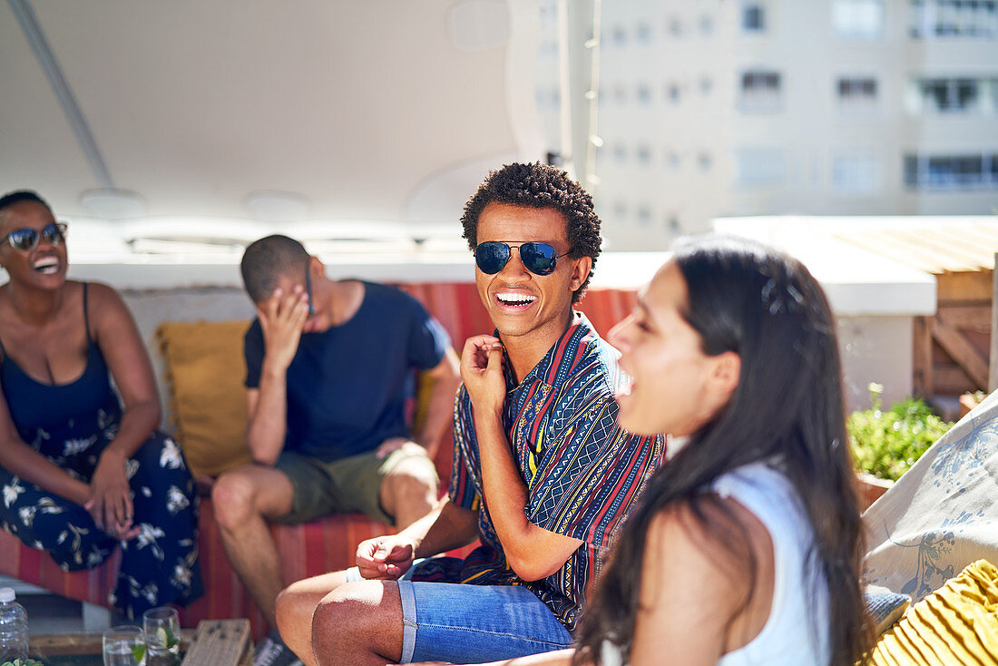 Happy young friends laughing on sunny rooftop balcony