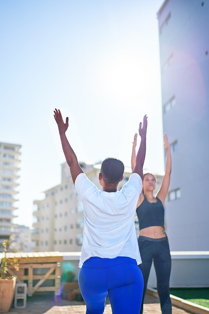 Young women practicing yoga on sunny urban rooftop balcony