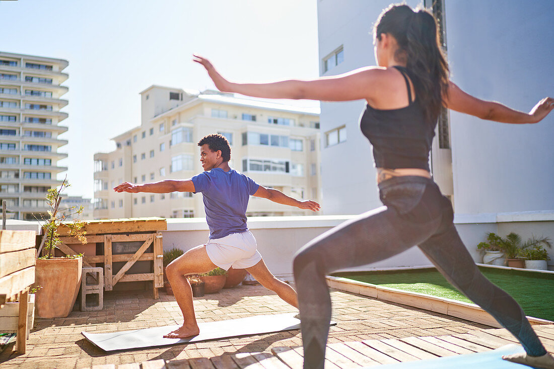 Young couple practicing yoga on sunny urban balcony rooftop