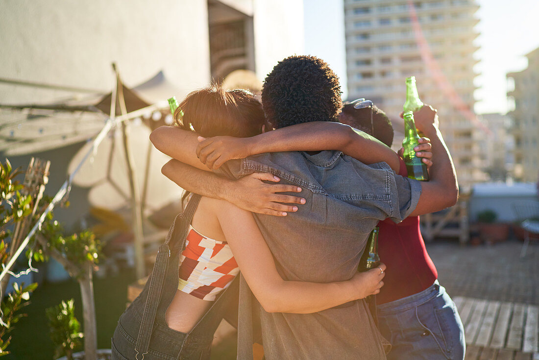 Happy young friends hugging and drinking beer on rooftop