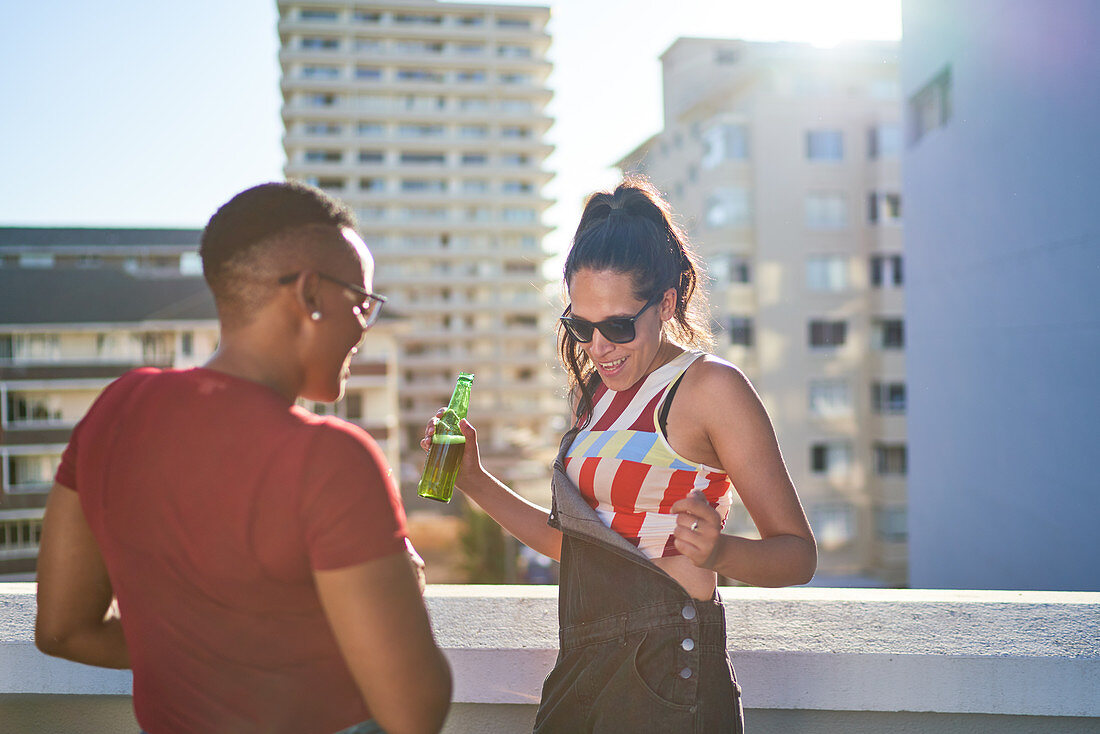 Carefree young woman dancing and drinking beer on rooftop