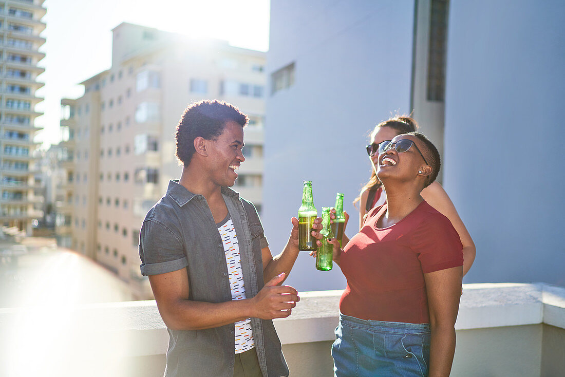 Happy young friends drinking beer on sunny rooftop balcony