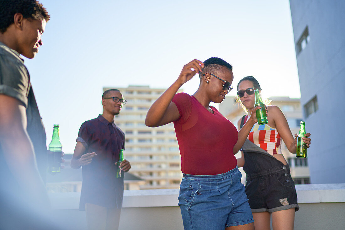 Carefree young friends dancing and drinking beer on rooftop
