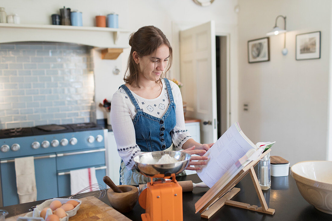 Teenage girl with cookbook baking in kitchen