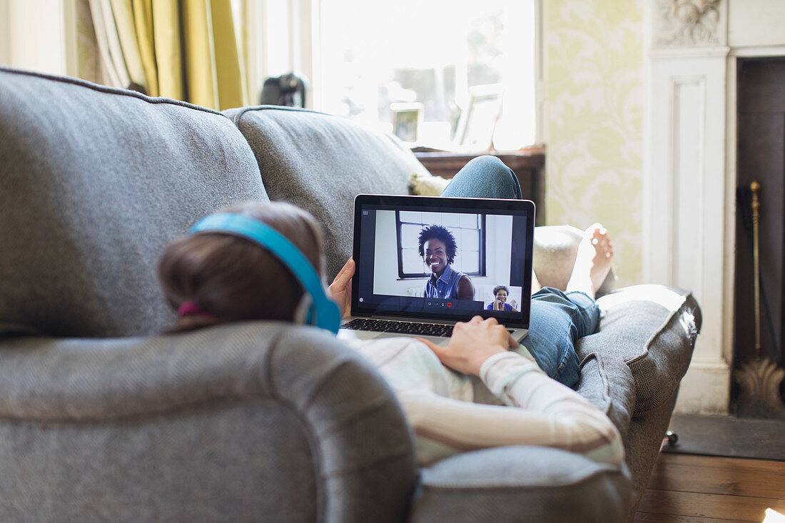 Teenage girl video chatting with friends on living room sofa