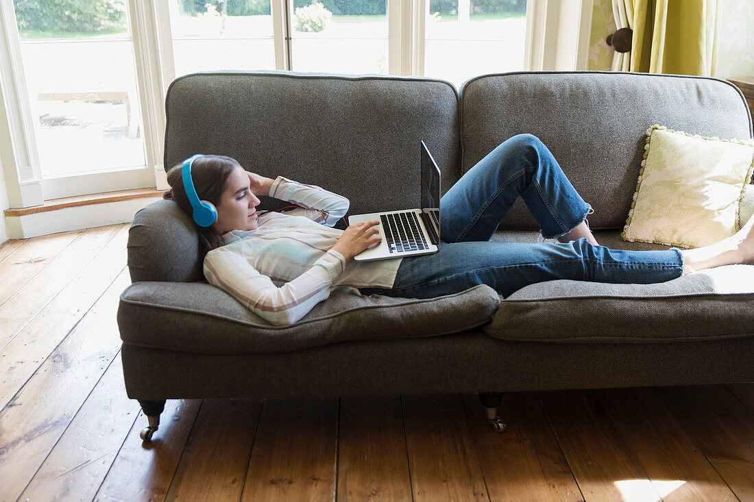 Teenage girl with headphones video chatting on sofa