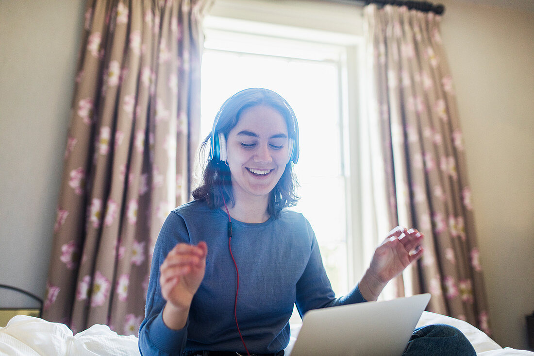 Teenage girl with headphones listening music on bed