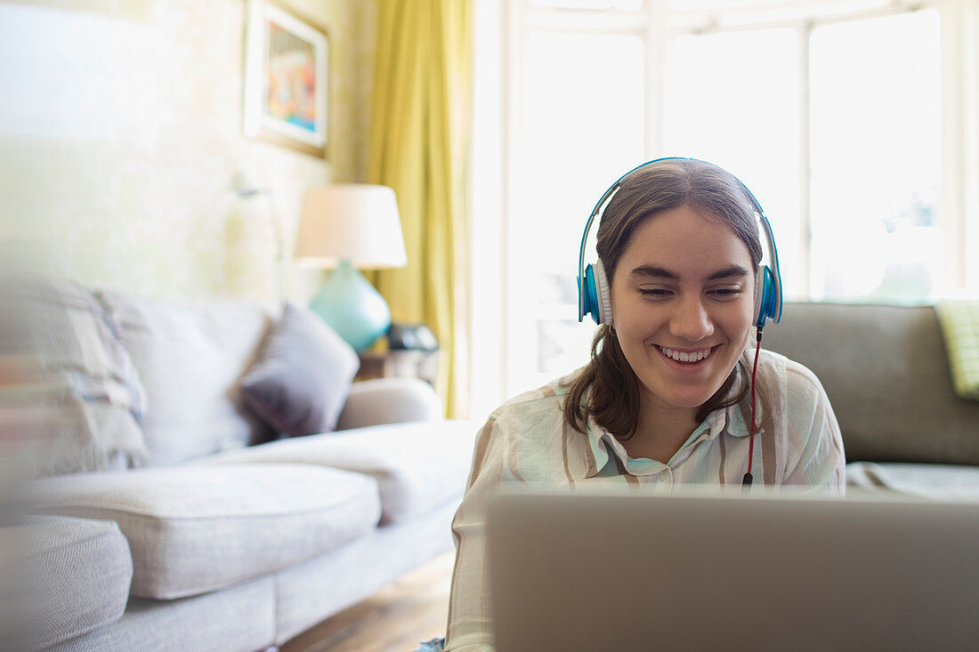 Teenage girl with headphones using laptop in living room