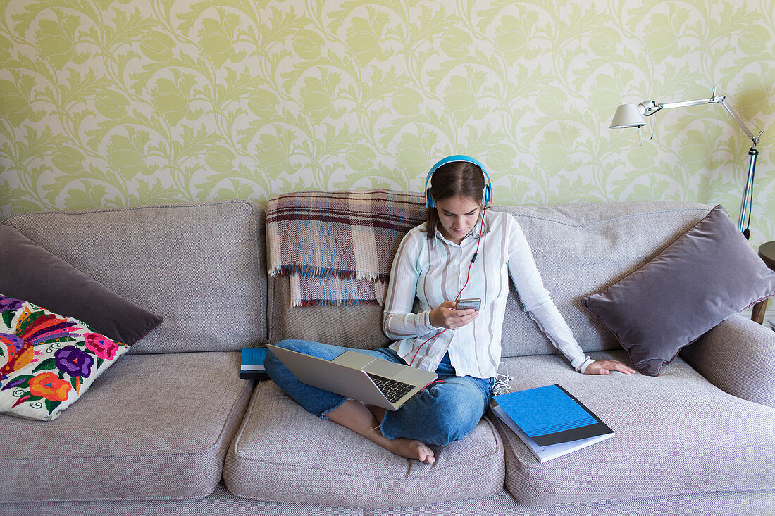 Teenage girl with headphones using smart phone on sofa