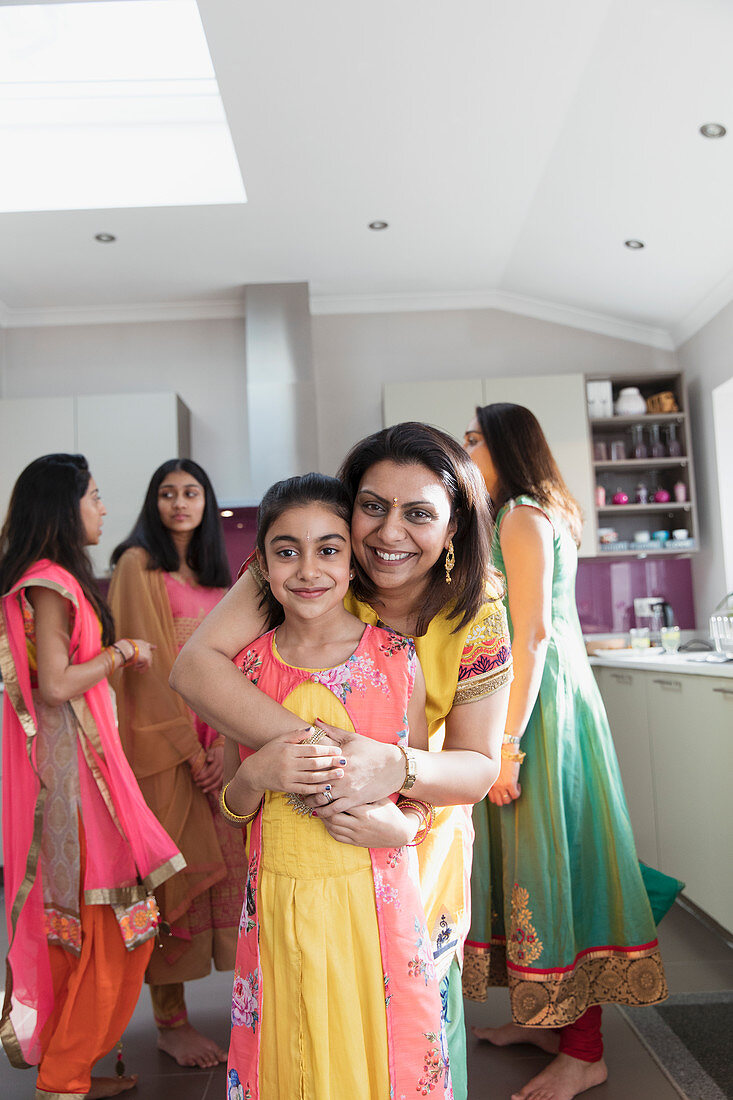 Happy Indian mother and daughter in saris hugging in kitchen
