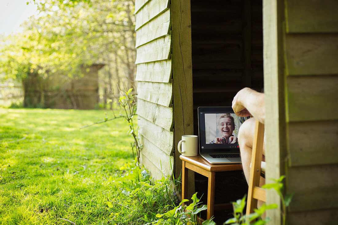 Man video chatting with friends on laptop from garden shed