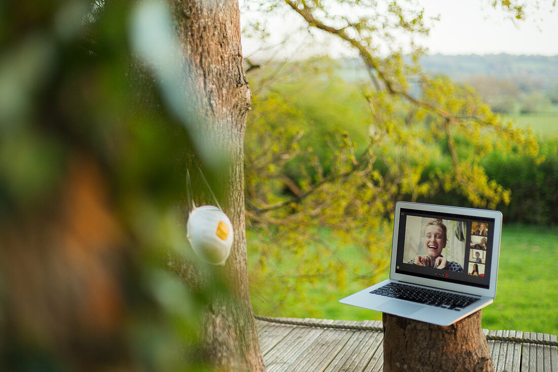Face mask hanging on tree next to friends video chatting