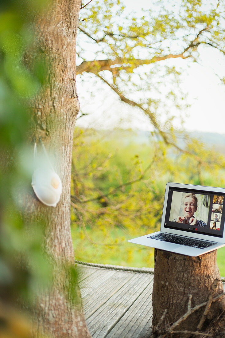 Face mask hanging on tree near friends video chatting
