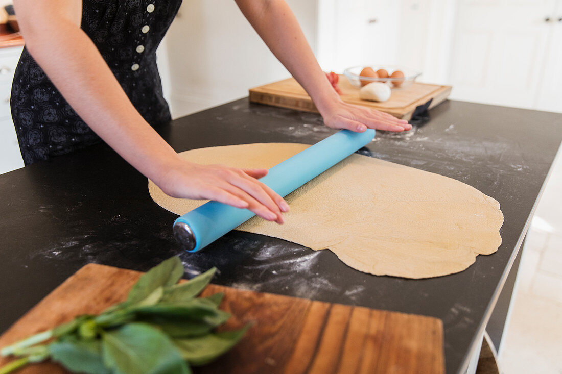 Teenage girl rolling out dough on kitchen counter