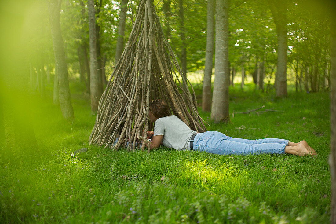 Woman laying at branch teepee in woodland