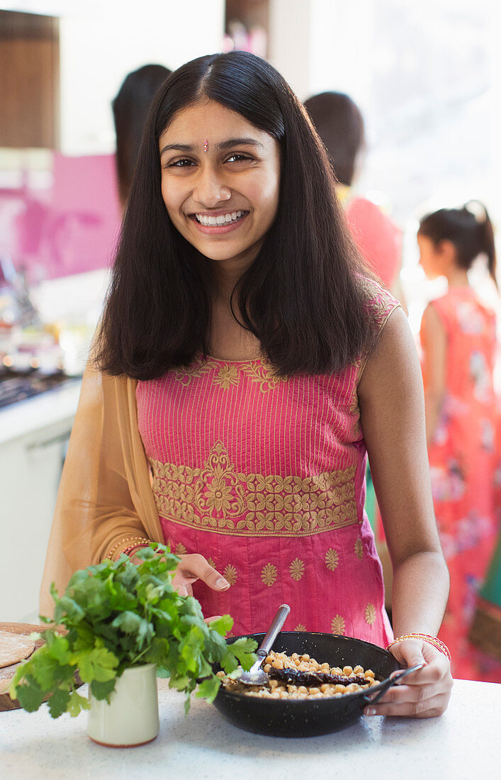 Portrait smiling Indian girl in sari eating in kitchen