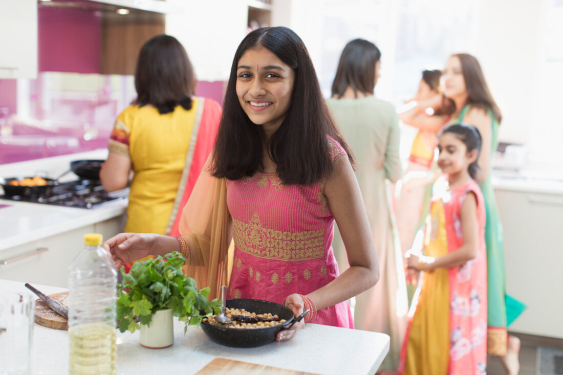 Portrait happy Indian girl in sari cooking food in kitchen