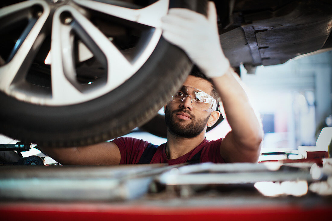 Male mechanic working under car, examining tire