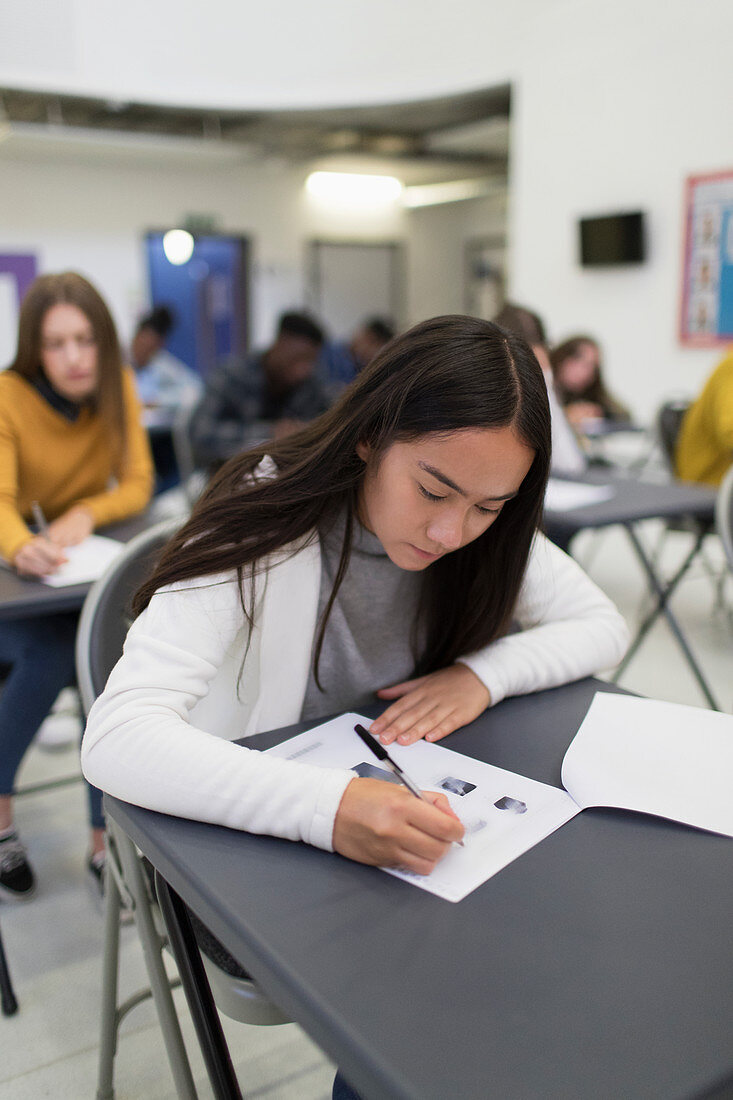 High school girl taking exam at desk in classroom