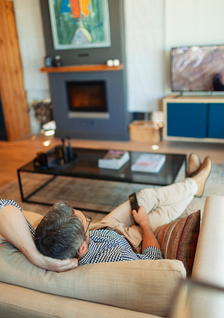 Man relaxing, watching TV on living room sofa