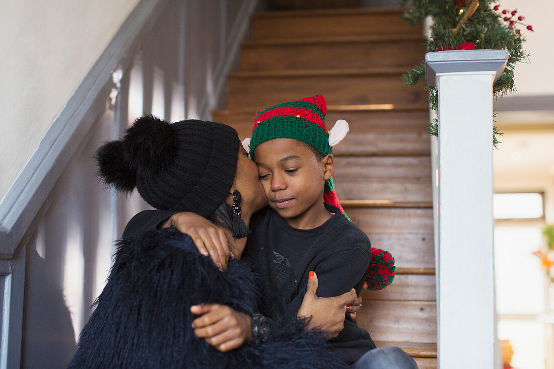 Mother kissing son in Christmas hat on stairs