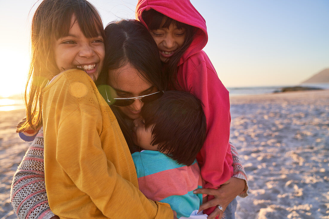 Happy mother and kids hugging on sunny beach