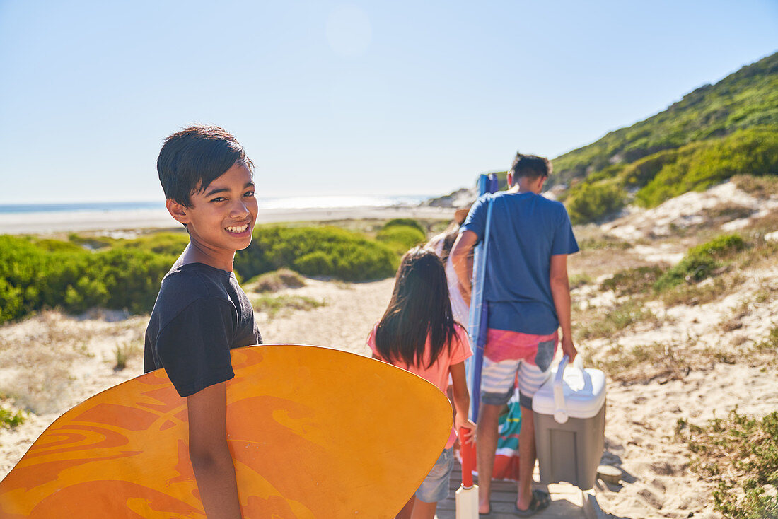 Portrait boy carrying bodyboard on sunny beach