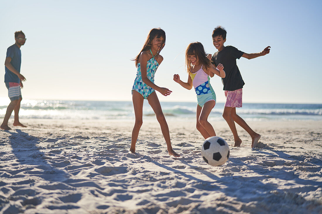 Happy family playing soccer on sunny beach