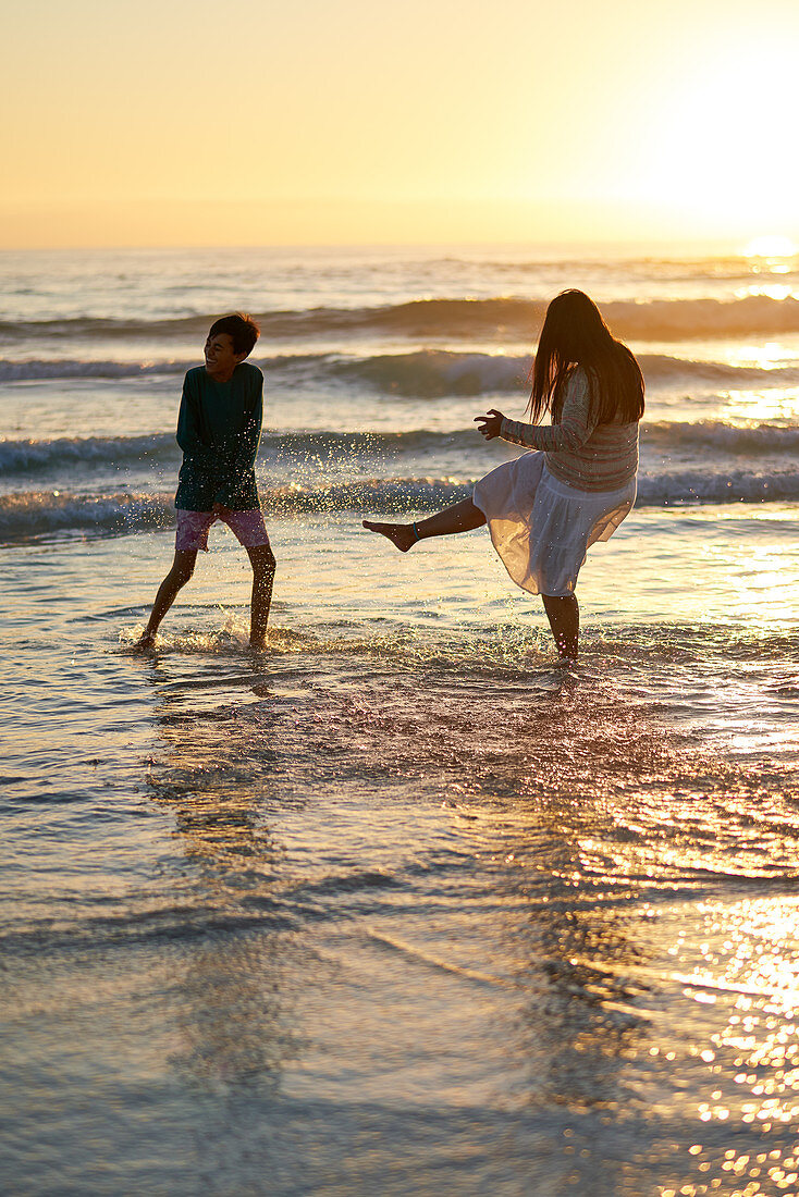 Mother and son splashing in ocean surf at sunset
